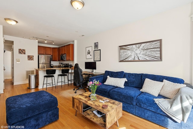 living area with track lighting, visible vents, light wood-type flooring, and baseboards