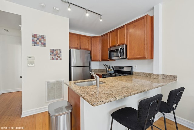 kitchen with visible vents, light wood finished floors, a peninsula, a sink, and appliances with stainless steel finishes