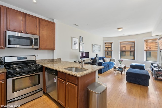 kitchen featuring light wood-style flooring, a sink, open floor plan, stainless steel appliances, and a peninsula