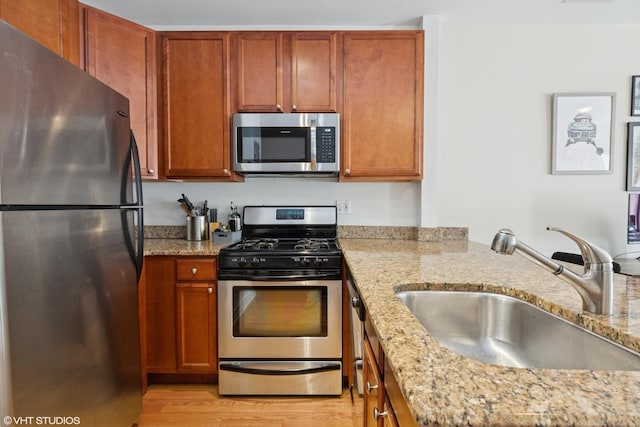 kitchen featuring light stone counters, brown cabinetry, a sink, stainless steel appliances, and light wood-style floors