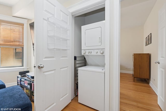 clothes washing area with stacked washer / drying machine, baseboards, laundry area, and light wood finished floors