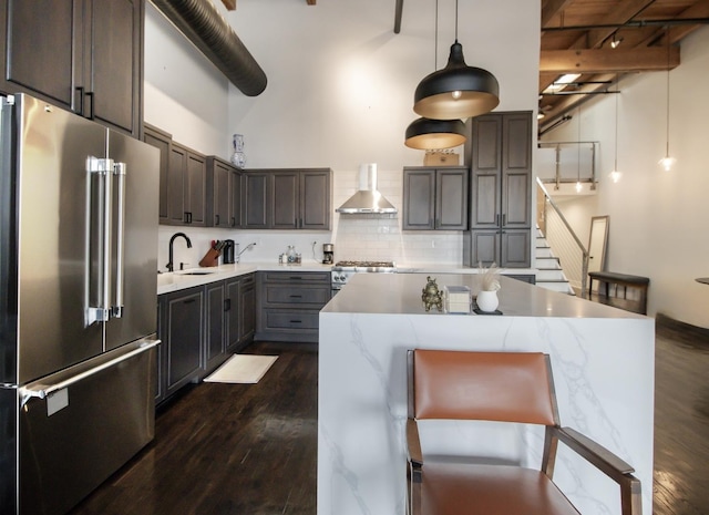 kitchen featuring tasteful backsplash, wall chimney range hood, a towering ceiling, stainless steel appliances, and a sink