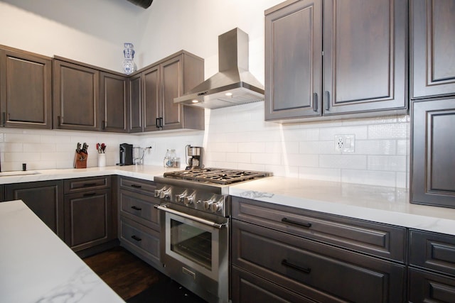 kitchen with backsplash, high end stove, dark brown cabinetry, and wall chimney exhaust hood