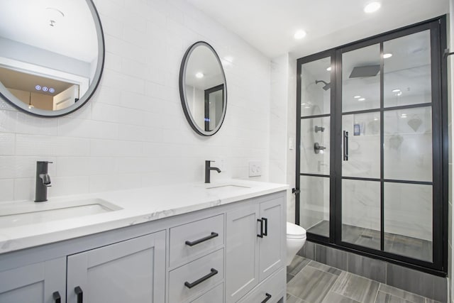 full bathroom featuring a sink, tile walls, a shower stall, and double vanity