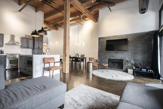 living area featuring beam ceiling, a high ceiling, a stone fireplace, and dark wood-style flooring