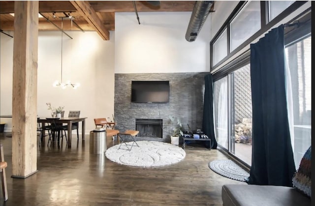 living area with a stone fireplace, a high ceiling, a notable chandelier, and wood finished floors