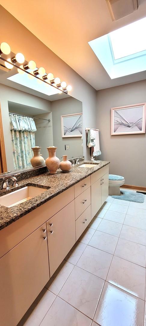 bathroom with toilet, a sink, a skylight, tile patterned flooring, and double vanity