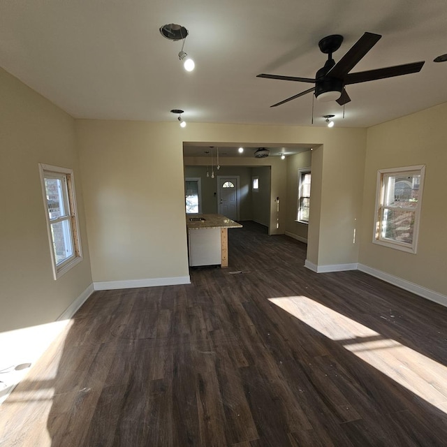 unfurnished living room with baseboards, dark wood-type flooring, and a ceiling fan