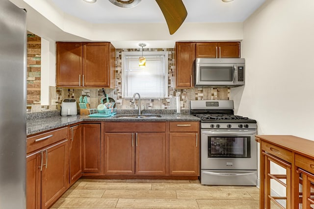 kitchen featuring wood finish floors, dark stone counters, decorative backsplash, appliances with stainless steel finishes, and a sink