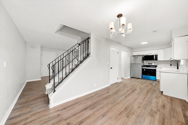 kitchen with a sink, stainless steel appliances, white cabinets, light wood finished floors, and baseboards