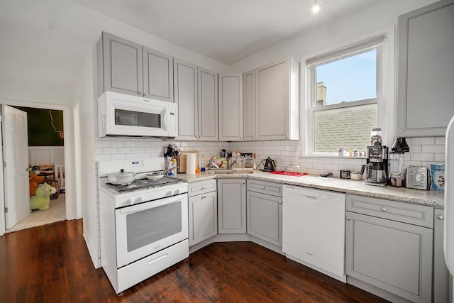 kitchen with gray cabinetry, a sink, tasteful backsplash, dark wood finished floors, and white appliances