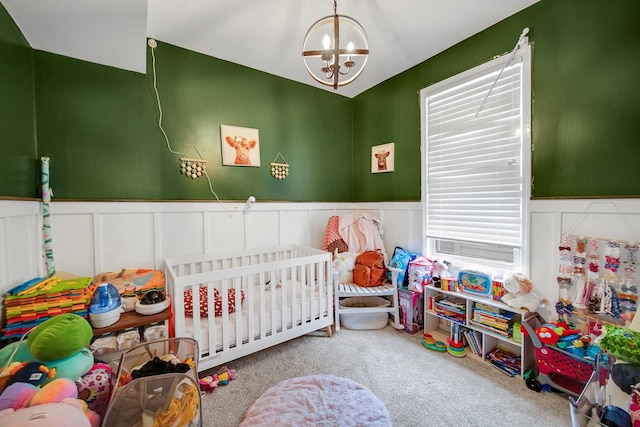 carpeted bedroom featuring wainscoting, a crib, and an inviting chandelier