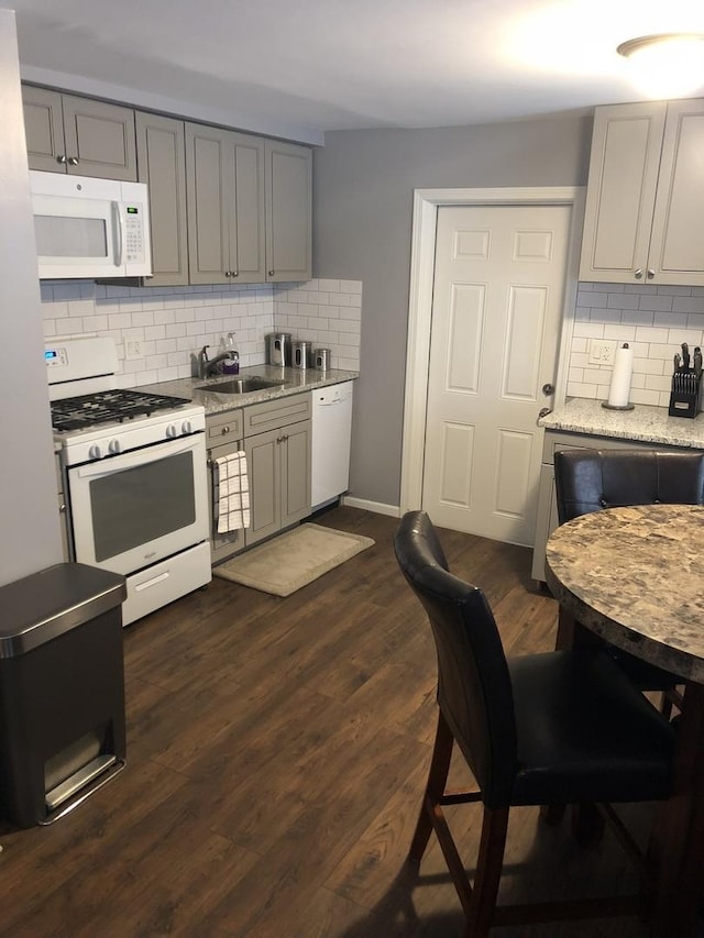 kitchen featuring white appliances, gray cabinets, dark wood-type flooring, and a sink