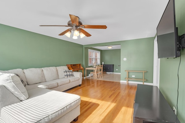 living room featuring a ceiling fan, baseboards, and light wood finished floors