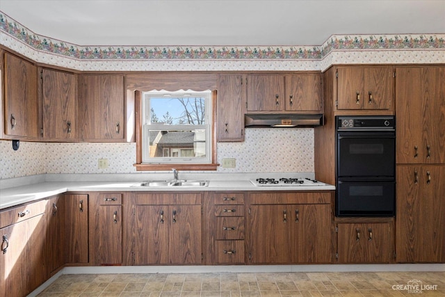 kitchen with dobule oven black, a sink, wall chimney range hood, wallpapered walls, and white gas cooktop