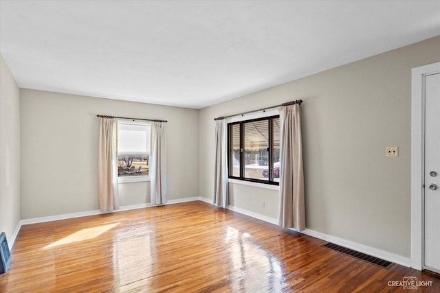 unfurnished room featuring wood finished floors, visible vents, and baseboards