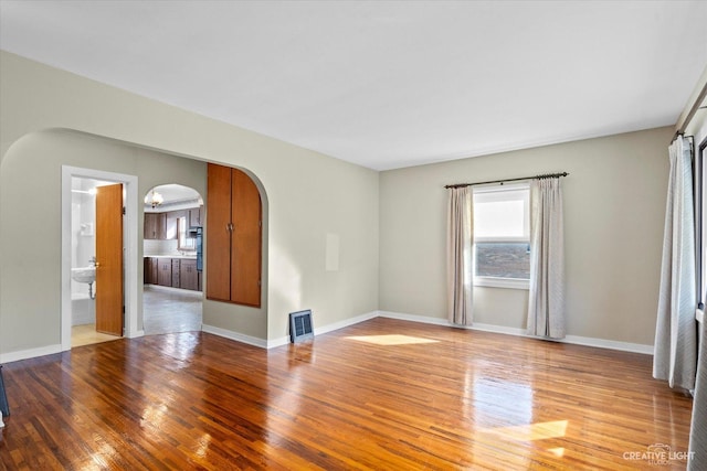 unfurnished room featuring visible vents, arched walkways, baseboards, and wood finished floors