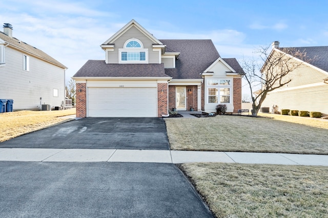 traditional home with central air condition unit, an attached garage, brick siding, and driveway