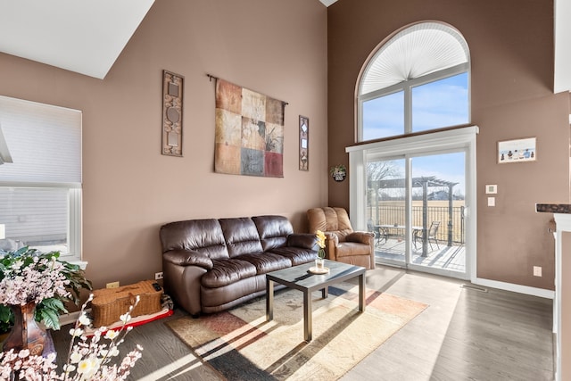 living room with a high ceiling, baseboards, and light wood-type flooring