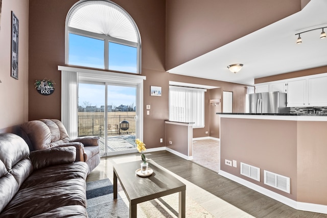 living area with visible vents, baseboards, rail lighting, a high ceiling, and wood finished floors