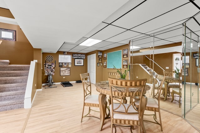 dining space featuring stairs, light wood-style floors, baseboards, and a drop ceiling