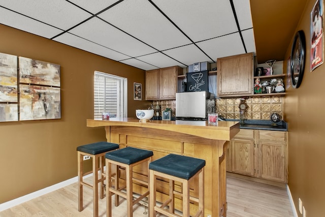 kitchen featuring a kitchen bar, open shelves, light wood-style flooring, and a drop ceiling