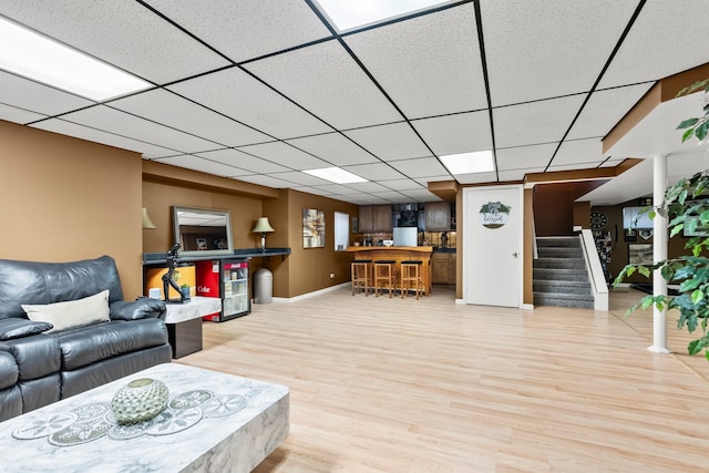 living area featuring stairs, wood finished floors, baseboards, and a drop ceiling