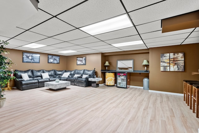 living room featuring beverage cooler, wood finished floors, baseboards, and a paneled ceiling