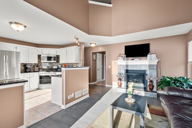 kitchen with open floor plan, decorative backsplash, a tile fireplace, appliances with stainless steel finishes, and white cabinetry