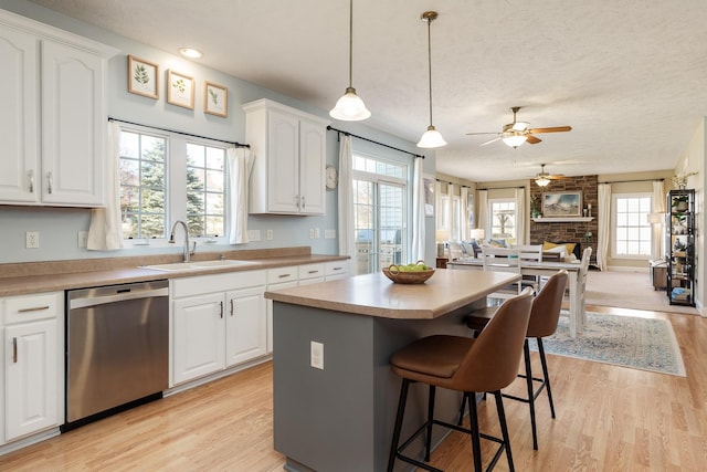 kitchen with open floor plan, stainless steel dishwasher, light wood-style floors, white cabinets, and a sink