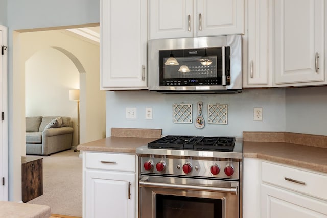 kitchen with stainless steel appliances, arched walkways, white cabinets, and carpet flooring