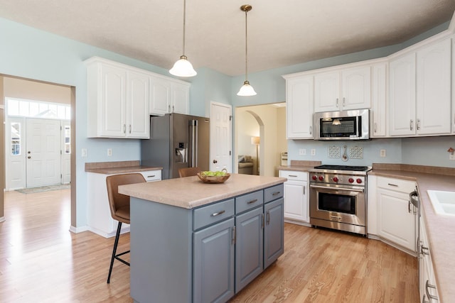 kitchen featuring high end appliances, light wood finished floors, arched walkways, gray cabinetry, and white cabinetry