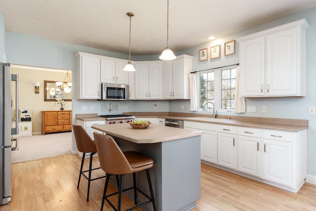 kitchen with a breakfast bar, a sink, appliances with stainless steel finishes, white cabinetry, and light wood-type flooring