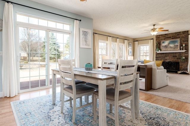 dining room with ceiling fan, light wood-style flooring, a fireplace, and a textured ceiling