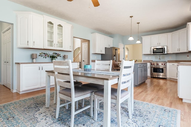 kitchen featuring light wood finished floors, glass insert cabinets, high quality appliances, arched walkways, and white cabinets