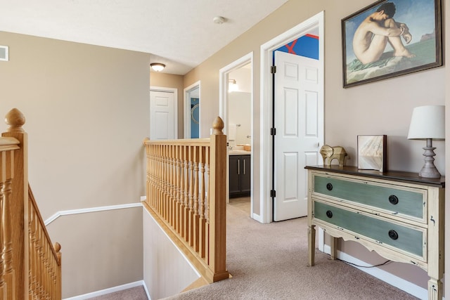 hallway featuring visible vents, an upstairs landing, light colored carpet, and baseboards