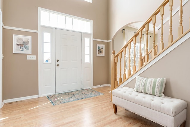 foyer featuring baseboards, stairway, a high ceiling, wood finished floors, and arched walkways