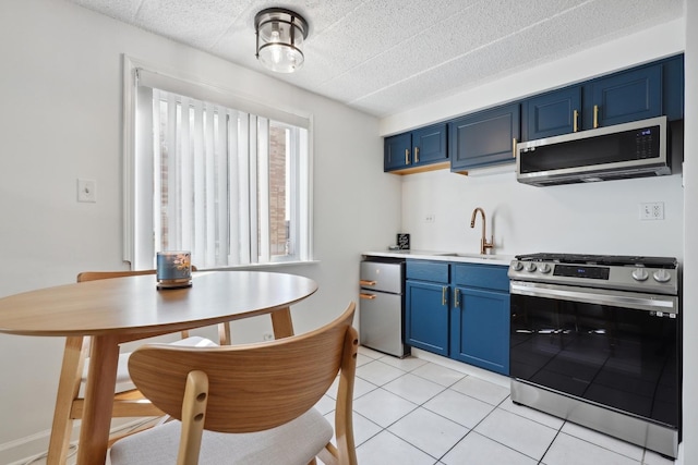 kitchen with blue cabinetry, a sink, stainless steel appliances, light tile patterned flooring, and light countertops