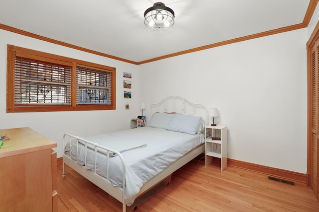 bedroom featuring light wood finished floors, visible vents, baseboards, and ornamental molding