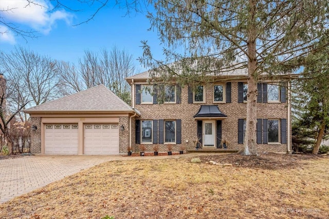 colonial house with decorative driveway, an attached garage, and brick siding