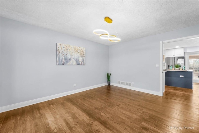 empty room with visible vents, baseboards, a textured ceiling, and wood finished floors