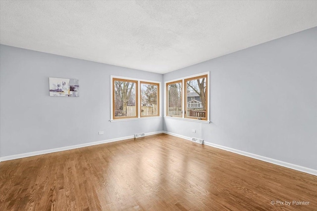 unfurnished room with visible vents, baseboards, a textured ceiling, and wood finished floors