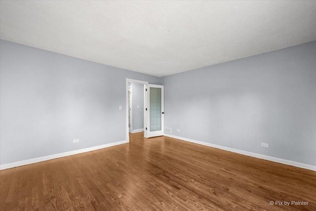 unfurnished room featuring visible vents, a textured ceiling, baseboards, and wood finished floors