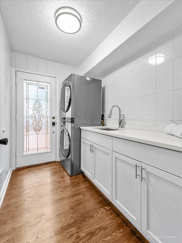 clothes washing area with stacked washing maching and dryer, wood finished floors, cabinet space, a textured ceiling, and a sink