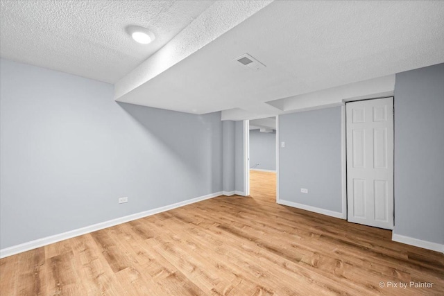 finished below grade area featuring visible vents, baseboards, light wood-style floors, and a textured ceiling