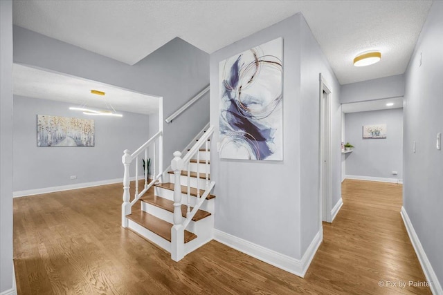 stairs with wood finished floors, baseboards, and a textured ceiling