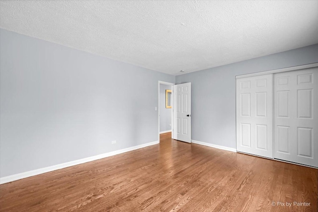 unfurnished bedroom featuring a closet, baseboards, a textured ceiling, and wood finished floors