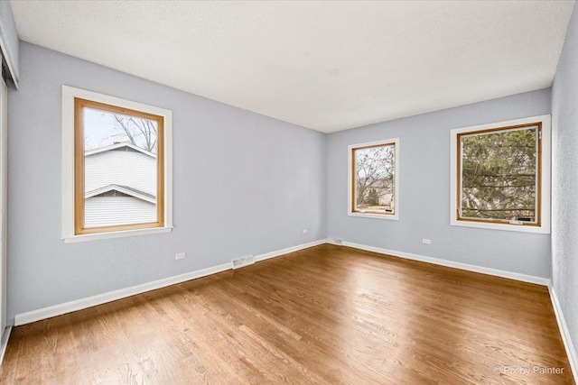 unfurnished room with a wealth of natural light, visible vents, baseboards, and wood finished floors