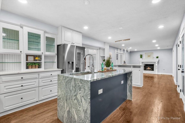 kitchen with dark wood finished floors, a center island with sink, stainless steel fridge, and white cabinetry