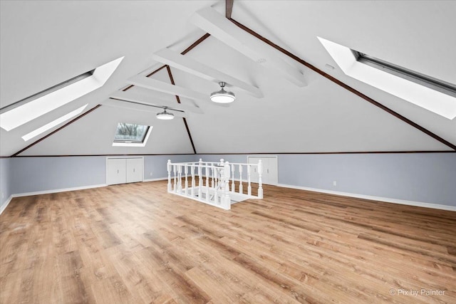 additional living space with vaulted ceiling with skylight, wood finished floors, and baseboards